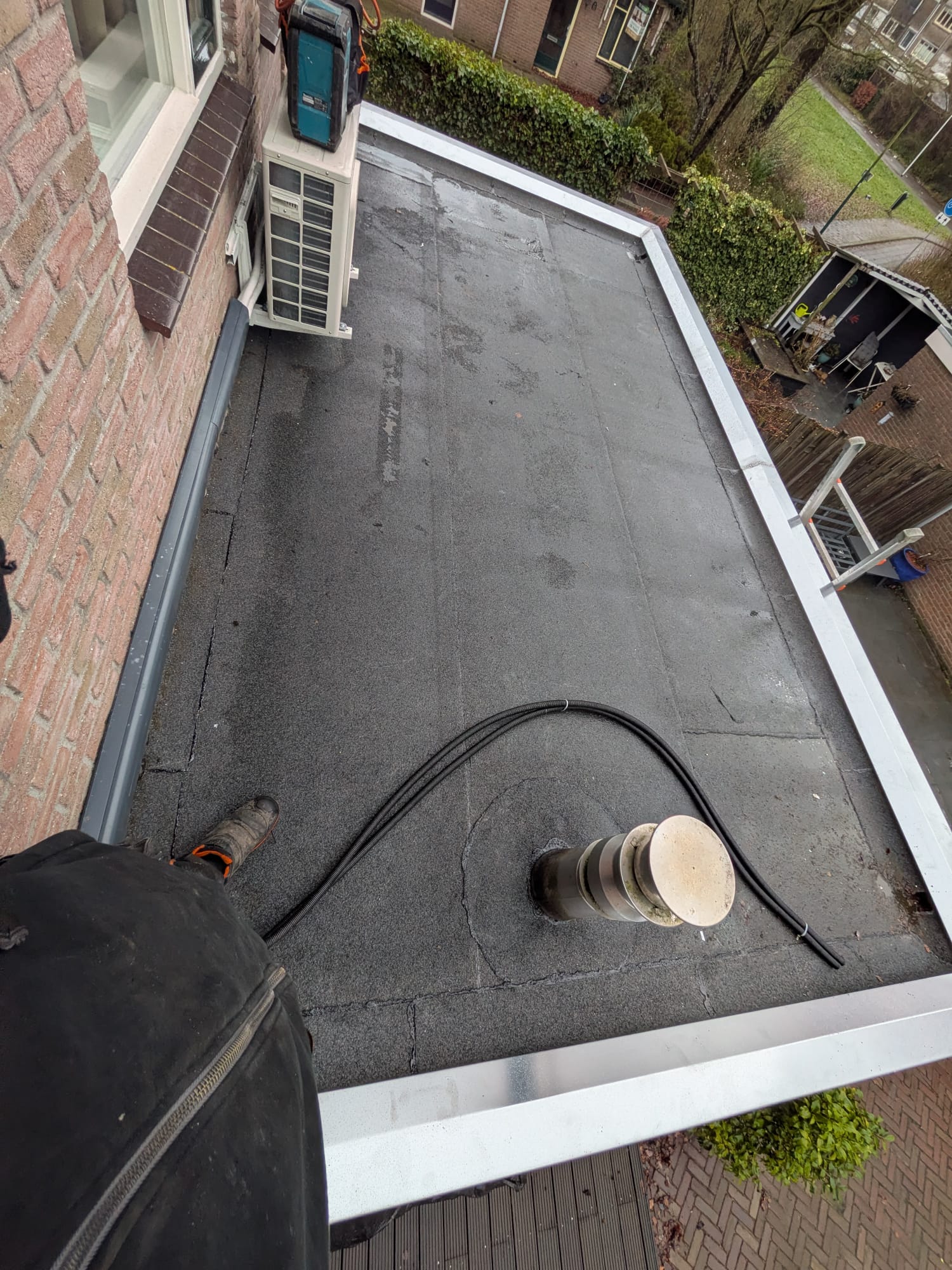 Plat dak met airconditioner en ventilatiepijp in regen.