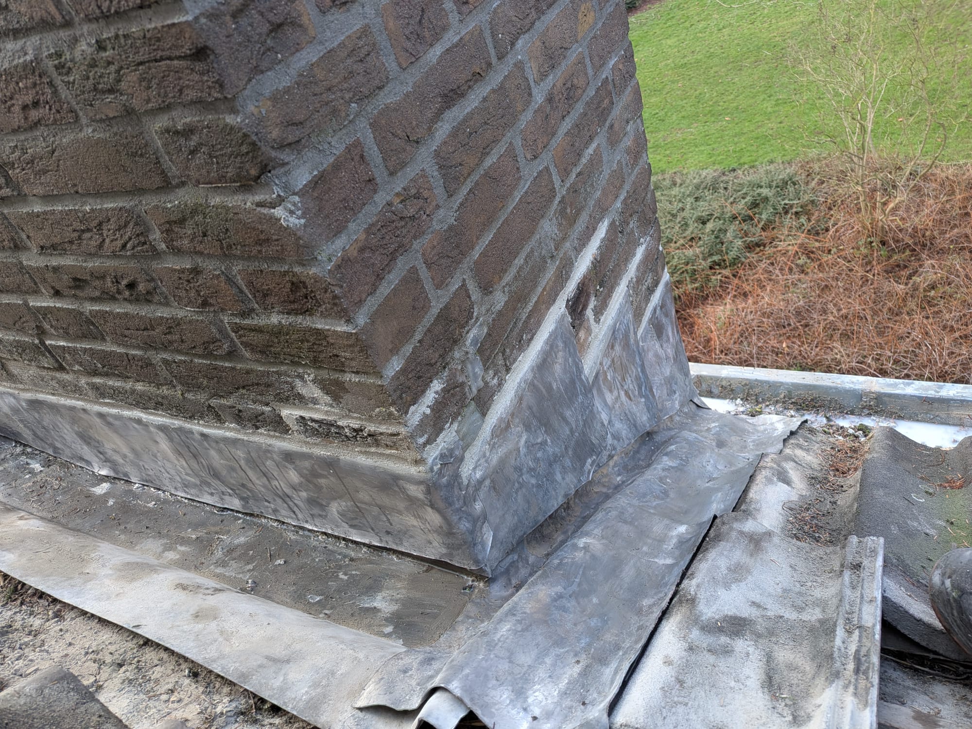 Bakstenen schoorsteen met loodslab op dakrand.